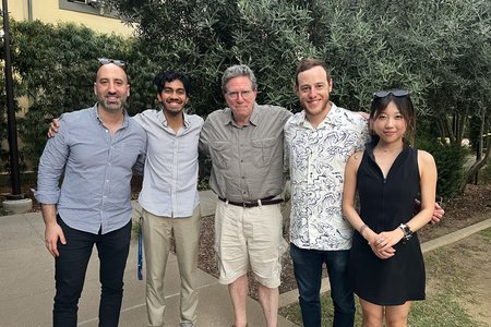 A group of five people standing with their arms around one another