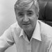 black and white photo of a man with grey hair sitting wearing a white button-up shirt, sitting in a chair