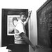 A black and white photo of a man at the blackboard with a chemistry calculation on the board.