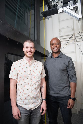 A photo of Simon Anuszczyk and John Dabiri. They both smile and stand in front of a large tank of water.