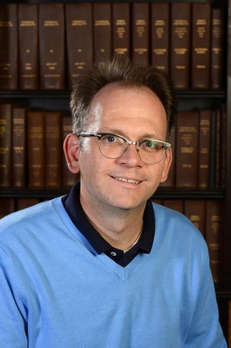 Brian Stoltz in front of a bookshelf.