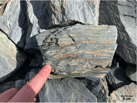 A person's finger points to stripes on a rock