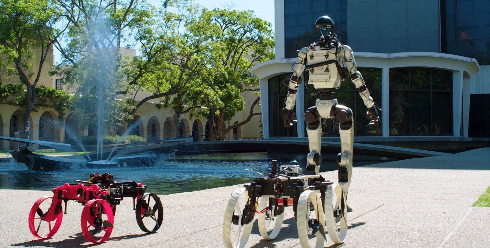 a humanoid robot and two rolling robots in front of Caltech Hall and its fountain at Caltech