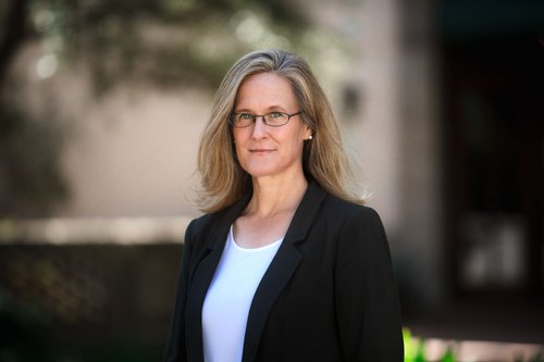 A portrait of Tracy Dennison. She is outside and wears a blazer.