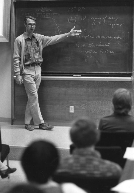 A man standing next to a blackboard in a lecture hall