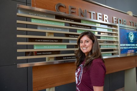 A person smiles, standing in front of a sign.