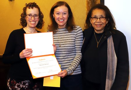 Three women pose for a photo with an award