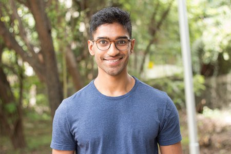 A portrait of Eshaan Patheria. He wears glasses and a T-shirt and smiles at the camera.