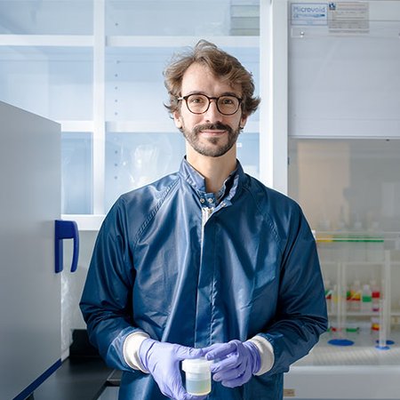 Francois Tissot of Caltech in a lab setting, wearing a blue lab coat and latex gloves