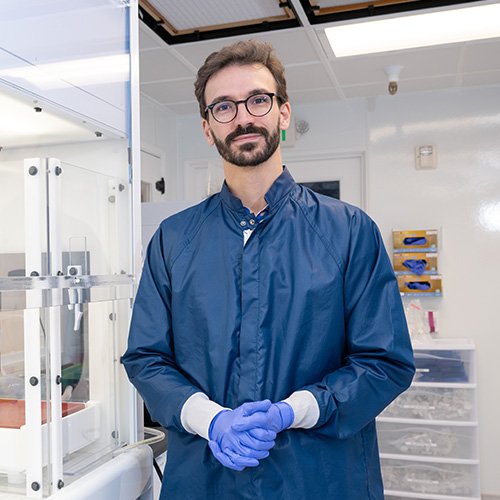 Francois Tissot of Caltech in a lab setting, wearing a blue lab coat and latex gloves