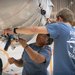 Two undergraduate students in blue shirts work with the wires underneath a white blimp.