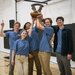 Five students in blue shirts hold up the gear trophy that goes to the ME72 champions each year.