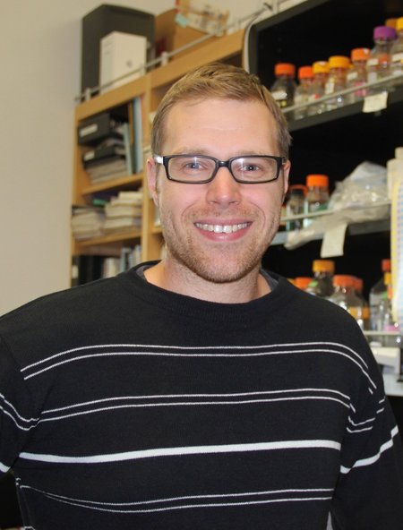 A person in a sweater smiles for a photo in a laboratory