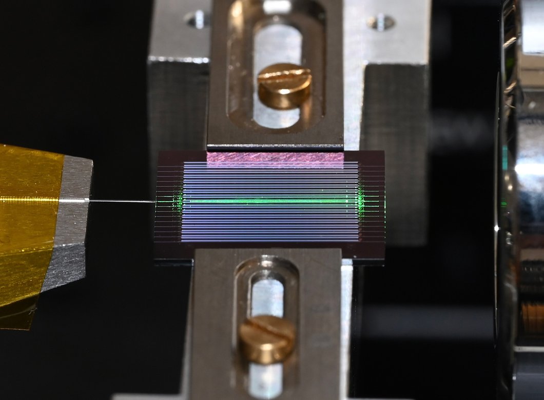 a chip with multiple horizontal channels has one lit up green. An optical fiber extends from the chip to the left.