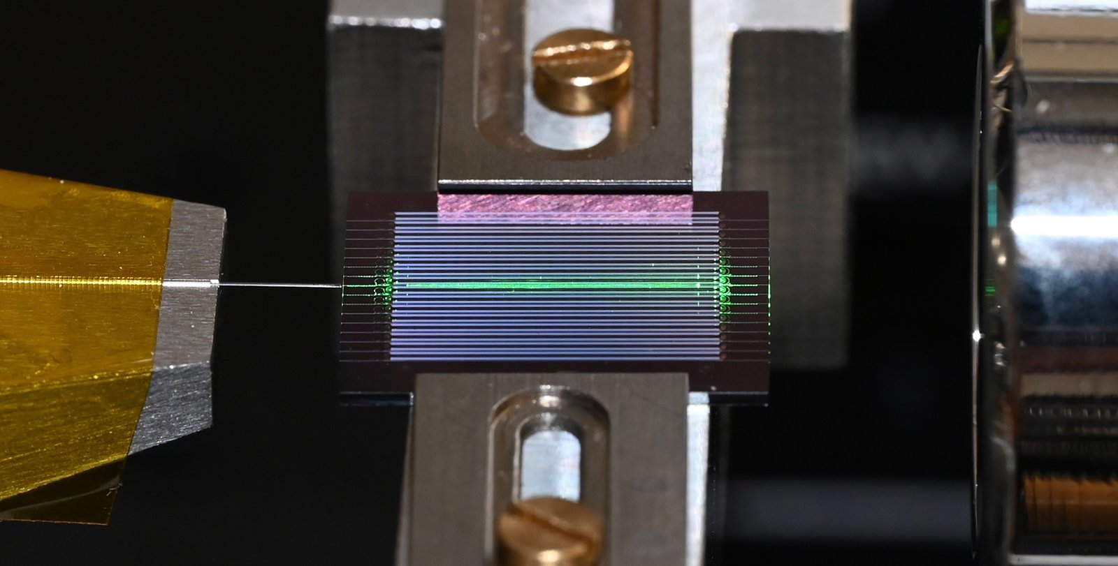 a chip with multiple horizontal channels has one lit up green. An optical fiber extends from the chip to the left.