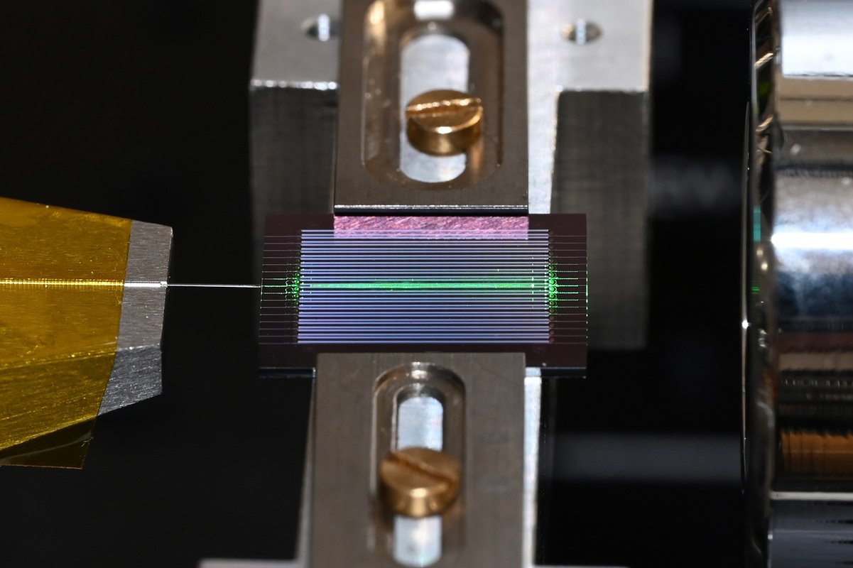 a chip with multiple horizontal channels has one lit up green. An optical fiber extends from the chip to the left.