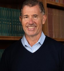 A portrait of R. Michael Alvarez. He stands in front of a book case and smiles.