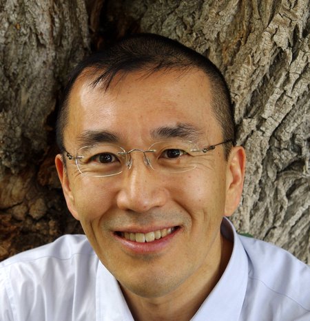 Close-up headshot of a man with glasses in front of tree bark