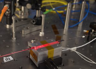 A red laser light shines through a flat waveguide on a metal workbench.