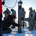 People in a snowy environment with a cylindrical instrument in the ground