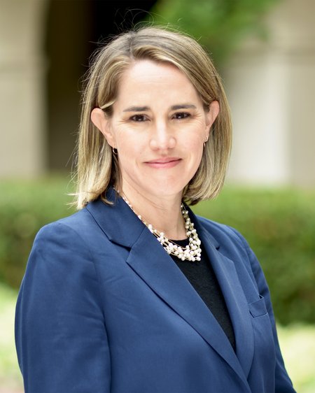 A photo portrait of a woman with blond hair wearing a blue blazer and black shirt with a chunky pearl necklace.