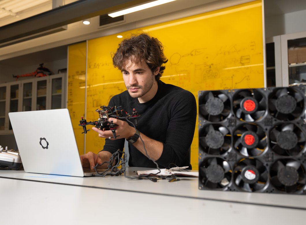 Alejandro Stefan-Zavala sits in front of a laptop with a drone in hand and small fans off to his side.