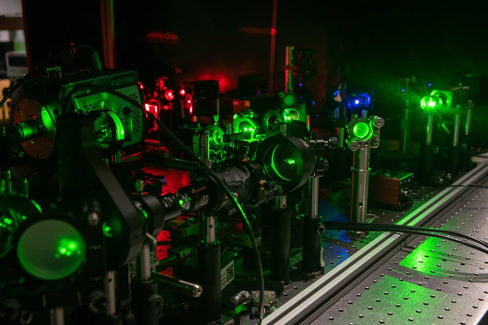 A photograph of the quantum microscopy apparatus. Green laser light shines through a series of lenses mounted to a table.