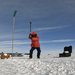 Zhongwen Zhan in a bright red winter coat swinging a sledgehammer at the Antarctic ice