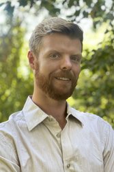 A portrait of Chris Kenseth. He is outdoors with trees in the background.